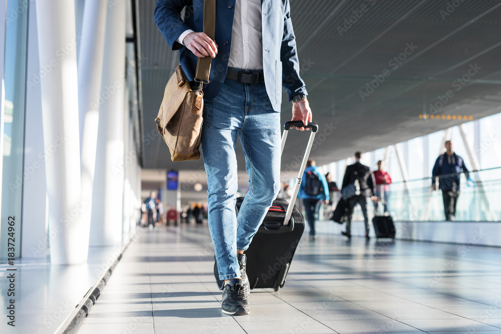 Man with shoulder bag and hand luggage walking in airport terminal